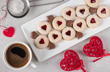 Homemade shortbread with raspberry jam heart-shaped filling and chocolate candies hearts on white plate on gray background