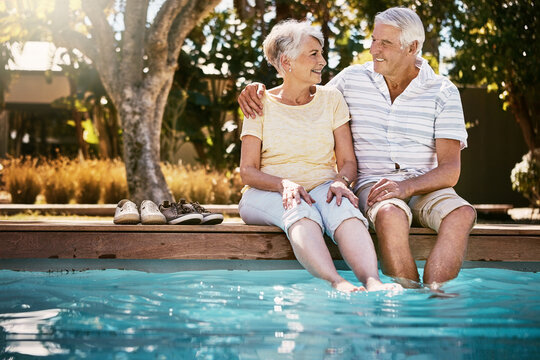 Senior couple, hug and swimming pool for holiday in relax for love or quality bonding time together on summer vacation. Happy elderly man holding woman relaxing with feet in water by the poolside