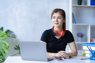 Smiling Asian student with headphones on his neck Study online with a teacher, learn a language, listen to a lecture, watch a webinar, write notes, look at a laptop at home. distance learning