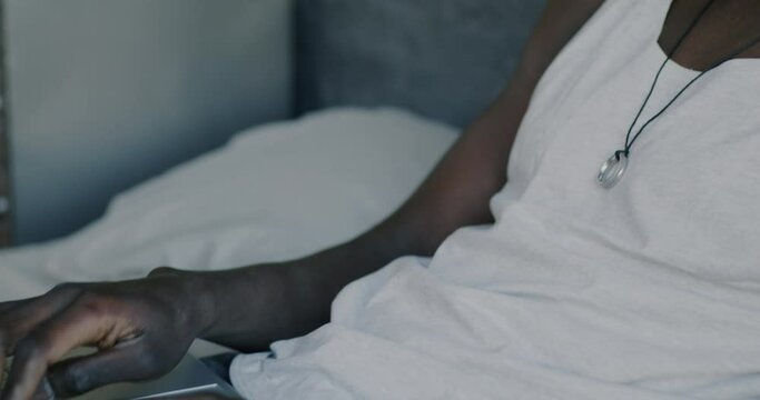 Tilt-up portrait of carefree African American man typing with laptop and laughing in bed at home. Online entertainment and modern technology concept.