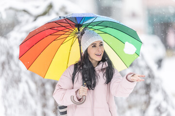 Happy woman holding an umbrella on a cold snowy day and throwing fresh snow