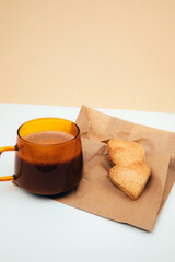 A cup of coffee with foam and a plate with heart-shaped shortbread cookies on a paper bag. Front view
