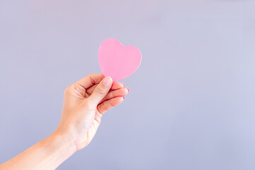 Fototapeta premium Woman hand holding a pink heart symbol. Hand holding a pink heart.The gesture symbolizes of love. Help and volunteering, Insurance health care, pink love and Valentine day concept.