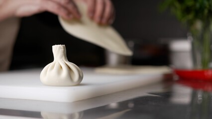 The chef's hands sculpt khinkali against the background of handmade cutting boards. Delicious homemade food, Georgian cuisine. Woman chef prepares khinkali in the restaurant kitchen.