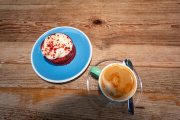 Imagen gastronómica de un café con leche en una taza verde y un pastel de red velvet en un plato azul sobre una mesa de madera.