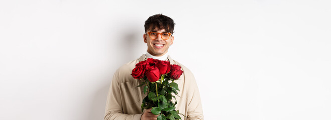 Handsome hipster guy waiting for his lover with bouquet of roses. Young man with flowers standing...