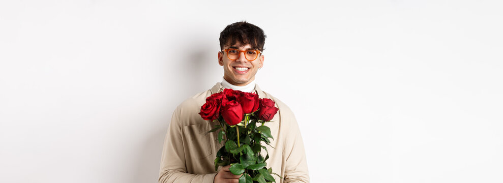 Handsome Hipster Guy Waiting For His Lover With Bouquet Of Roses. Young Man With Flowers Standing On Valentines Day Over White Background