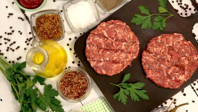 Round fresh raw mince beef burger cutlet with spices and sauce rotate on dark kitchen board.