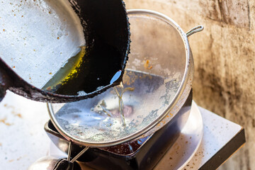 Pouring used cooking oil from frying pan into colander.