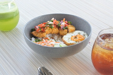 chicken katsu sambal matah with salad and sunny side up egg and drinks on a wooden table.