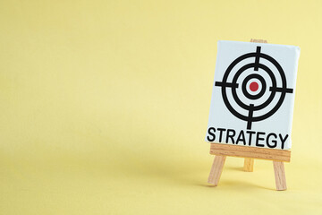 Target board icon with the word "strategy" on  standboard over yellow background with copyspace use for goal setting, target achievement, strategy, and progress tracking is important concept.