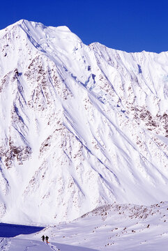 Pari of skiers touring beneath large mountain.