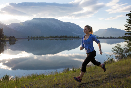 Young woman runs along edge of mtn lake, sunrise