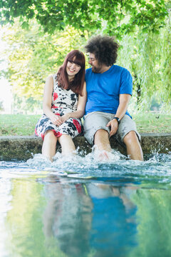Happy couple sitting with feet in water at Eisbach River