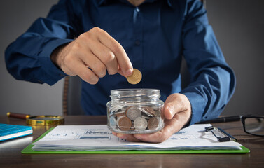 Businessman putting coin in glass bank. Saving money