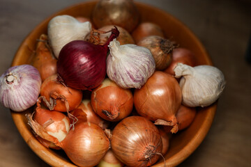 Onions and garlic. Brown and red onions and garlic clove in a wooden bowl on the table in the kitchen.