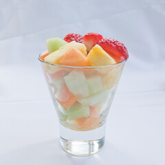 Fresh fruit salad in a clear glass cup on a white cloth background