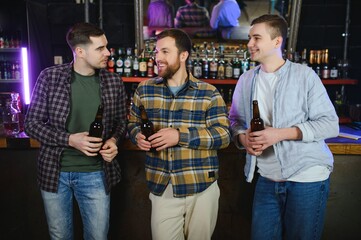 Young men in casual clothes are talking, laughing and drinking while sitting at bar counter in pub