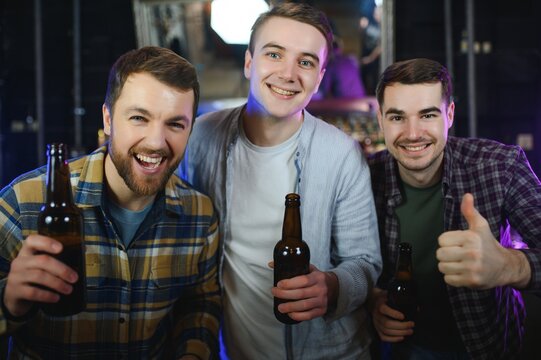 Young Men In Casual Clothes Are Talking, Laughing And Drinking While Sitting At Bar Counter In Pub