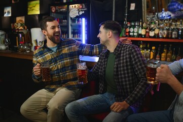 Fototapeta na wymiar Friends having fun. Happy young men in casual wear drinking beer in pub.