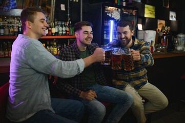 Old friends meeting. Happy young men in casual wear toasting with beer while sitting in beer pub together