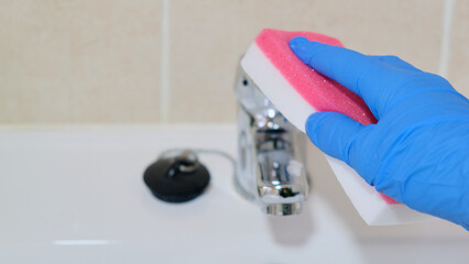Señora de la limpieza lavando grifo del cuarto de baño con un estropajo y guantes