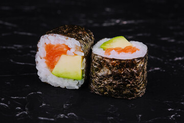 Sushi rolls with salmon and avocado on a black stone