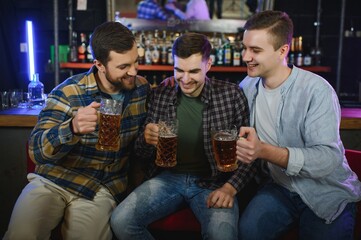 Young men in casual clothes are talking, laughing and drinking while sitting at bar counter in pub