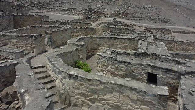 Drone shot of a 500 year old abandoned stone town on a rocky mountain side. Paths and stairs maze through the ruins. Drone flies forward above. Located in Lima, Peru in the district of Lurin.