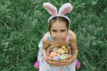 Easter egg hunt in spring garden. Funny girl with eggs basket and bunny ears on Easter egg hunt in garden. Children celebrating Easter. Happy easter card