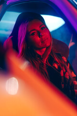 Portrait of beautiful young woman driving car at night in neon light.