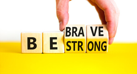 Be strong and brave symbol. Concept word Be strong Be brave on wooden cubes. Beautiful yellow table white background. Businessman hand. Business be strong and brave concept. Copy space.