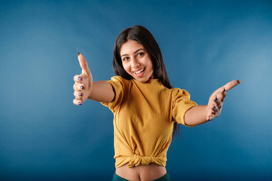 Young woman smiling confident isolated over blue background looking at the camera smiling with open arms for hug. Cheerful expression embracing happiness. Got some good news.