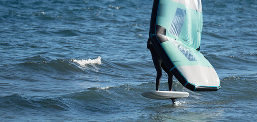 A man is wing foiling using handheld inflatable wings and hydrofoil surfboards in a blue ocean,...