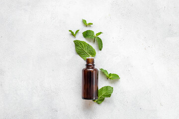 Bottle of essential peppermint oil with fresh green mint leaves