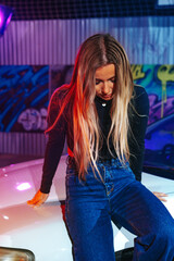 Young beautiful woman with straight long hair posing near white sport car in neon light