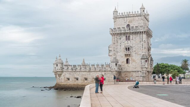 Belem Tower is a fortified tower located in the civil parish of Santa Maria de Belem timelapse in Lisbon, Portugal. People walking on waterfront at cloudy day