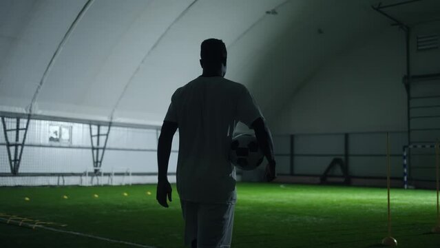 individual training of professional football player in indoor hall, rear view of african man