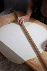 Fototapeta na wymiar Rolling dough using rolling pin. Women's hands in flour roll out the dough with a rolling pin on the table.