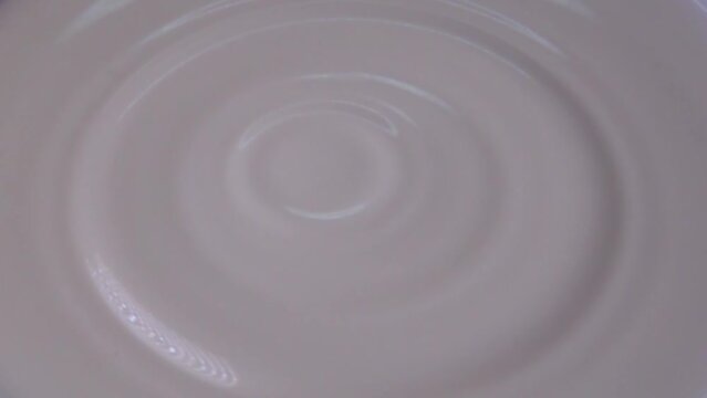 A drop of creamy white milk falls and forms ripples in slow motion
