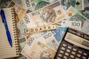 podatki - słowo ułożone z liter na tle banknotów, obok kalulaor, notes i długopis