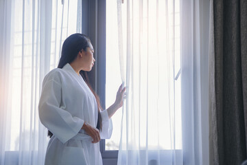 Woman in bathrobe suit waking up in modern bedroom open curtains enjoy morning sunrise. Life style and holiday concept.