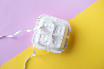 A small box with a wooden spoon tied with a white satin ribbon . Yellow and pink background