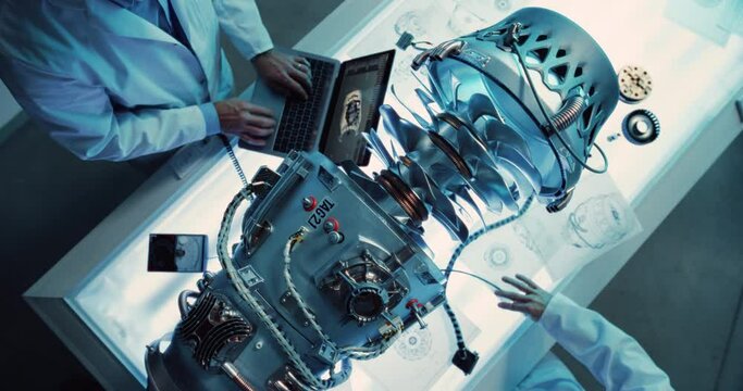 Two Professional Jet Engine Researchers Discussing Work, Using Laptop Computer and Checking Blueprints in Motor Manufacturing Facility. Scientists Researching Innovative Turbine Engine. Top Down View