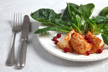 Grilled curd cheese mozzarella halloumi with green spinach and lingonberry cranberries with cutlery