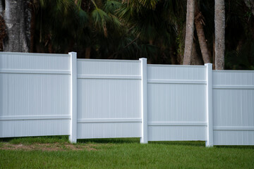 White vinyl picket fence on green lawn surrounding property grounds for backyard protection and...