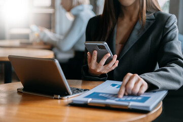 business documents on office table with smart phone and digital tablet and graph financial and woman working at office.