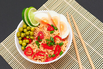 Beautiful Noodle Dish with Green Pea, Eggs, Red Hot Pepper, Greens and Lime with Chopsticks on Sushi Mat. Instant Noodles
