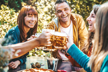 Happy friends cheering beer glasses in brewery pub garden - Group of happy people enjoying happy hour time sitting at bar table - Beverage, lifestyle and friendship concept