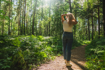 The young woman walks through a dark forest on a sunny day